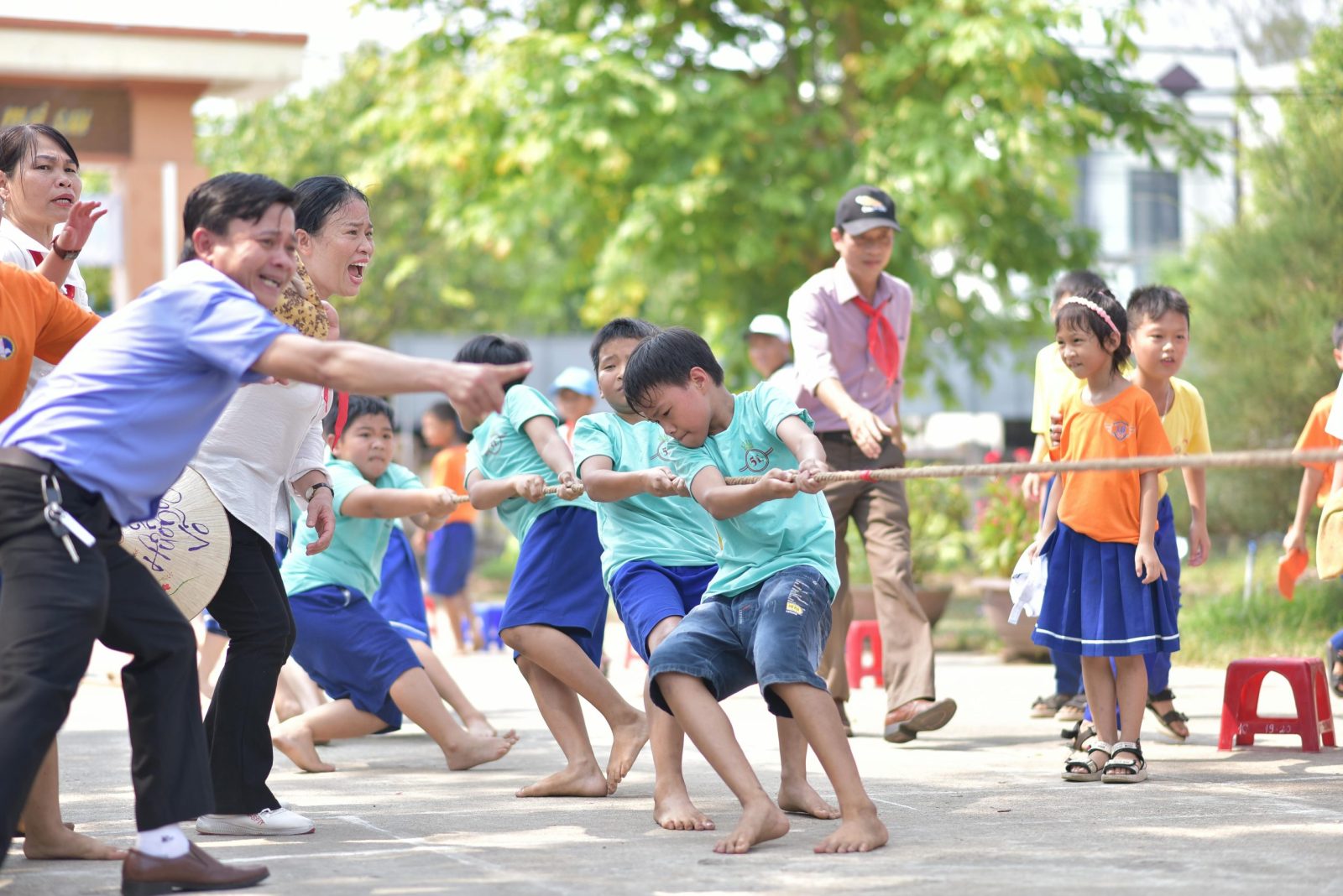 A lively tug-of-war game with children and adults outdoors under the sun. Perfect for depicting teamwork and fun.